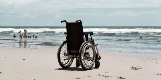 Leerer Rollstuhl am Strand, Meer im Hintergrund.
