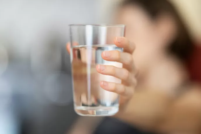 Hand hält Wasserglas, leicht verschwommen im Hintergrund Personen.
